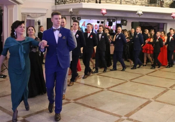 Grupa młodzieży w eleganckich garniturach i wieczorowych sukniach tańczy w balowej sali podczas balu przedmaturalnego w Gąbinie.