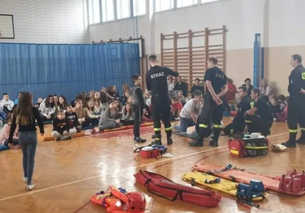 W sali gimnastycznej strażacy w czarnych uniformach z napisem Straż prezentują sprzęt ratowniczy przed zgromadzonymi uczniami podczas eliminacji gminnych Ogólnopolskiego Turnieju Wiedzy Pożarniczej.