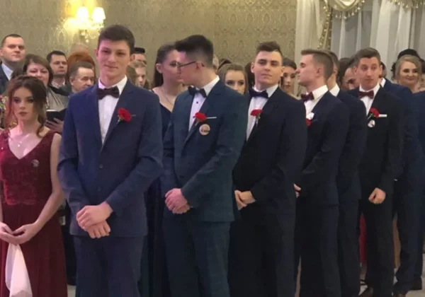 Grupa uczniów Zespołu Szkół im. Jana Śniadeckiego w Wyszogrodzie stoi w kolejce podczas studniówki, ubrani w eleganckie garnitury i wieczorowe suknie.
