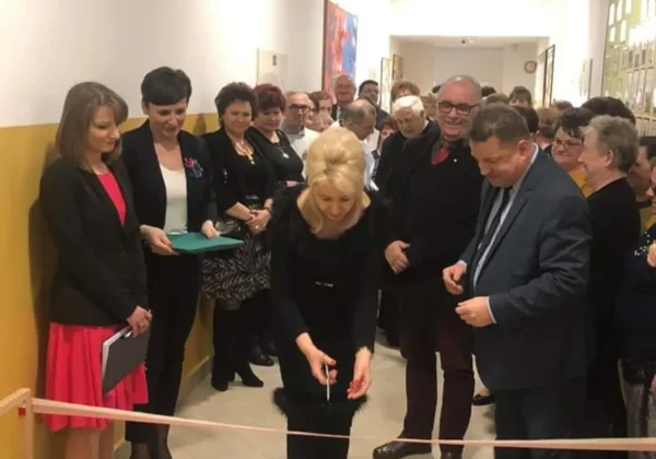 Grupa osób w formalnych ubraniach bierze udział w uroczystym przecięciu wstęgi na korytarzu podczas otwarcia Klubu Senior Plus w Soczewce.