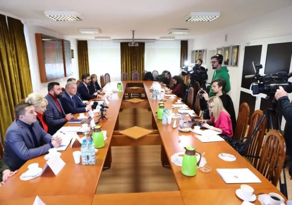 Konferencja prasowa w sali urzędu: urzędnicy i dziennikarze siedzą przy długim stołem ustawionym w literę U, a kamery i mikrofony skierowane są na relację dotyczące inwestycji drogowych, odbudowy DPS-u Nad Jarem i przekazania terenu w Trzepowie na rzecz Banku Żywności.