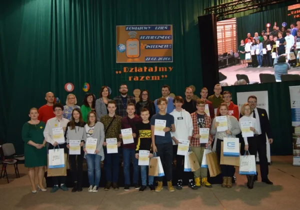 Grupa uczestników i organizatorów stoi na scenie podczas III Powiatowego Dnia Bezpiecznego Internetu 2020, wszyscy trzymają dyplomy i torby z upominkami.