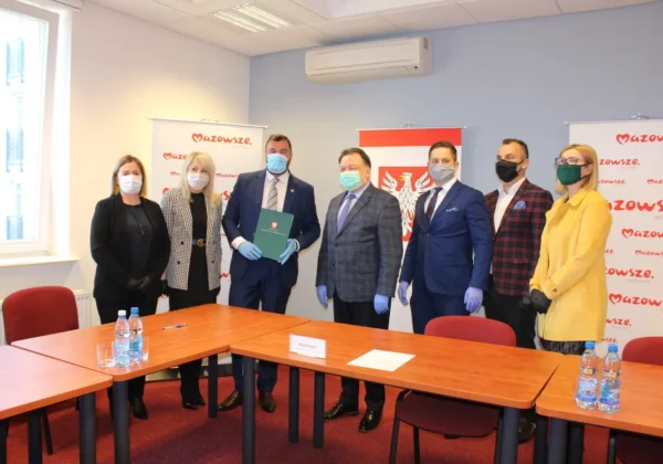 Grupa osób w maseczkach stoi przy stole podczas podpisywania umowy na odbudowę zniszczonego po pożarze DPS w Nowym Miszewie, na tle banerów Mazowsza.