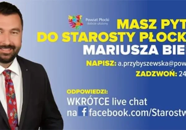 Na zdjęciu mężczyzna w garniturze stoi obok niebiesko‑żółtego plakatu informującego o możliwości zadania pytania staroście płockiemu oraz podanych kontaktach.