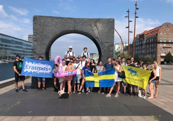 Grupa uczniów Zespołu Szkół im. Jana Śniadeckiego w Wyszogrodzie stoi na placu nad wodą, trzymając flagi Erasmus+, Ukrainy i Mobility Sweden podczas wyjazdu na praktyki w ramach programu Erasmus+ „Czas na Staż VOL 2”.