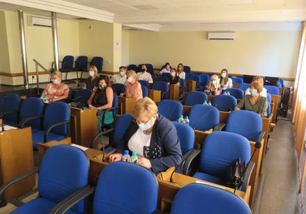 Sala konferencyjna z osobami w maseczkach siedzącymi w rozmieszczonych rzędach, pracującymi nad przygotowaniami szkół powiatowych do rozpoczęcia roku szkolnego w powiecie płockim.