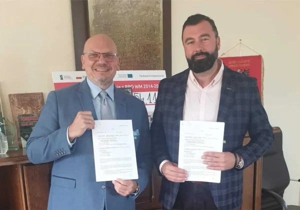 Dwóch mężczyzn w garniturach prezentuje podpisane dokumenty podczas spotkania dotyczącego powstania Strategii Elektromobilności Powiatu Płockiego.