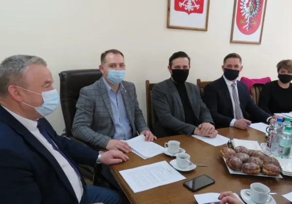 Kolejne posiedzenie Zarządu Powiatu Płockiego za nami: pięć osób w maseczkach siedzi przy stole z dokumentami i napojami, a na ścianie wiszą herby.