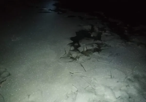 Nocny brzeg Wisły, pokryty lodem, z kamieniami i gałęziami na zimnym, błyszczącym podłożu.