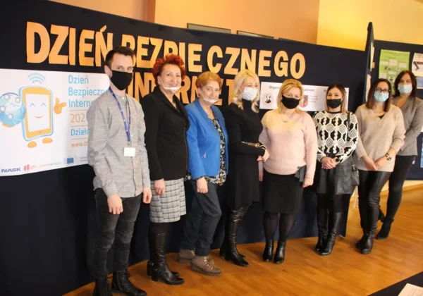 Grupa osób w maseczkach stoi razem przed dużym banerem z napisem Dzień Bezpiecznego Internetu 2021 – Działajmy Razem.