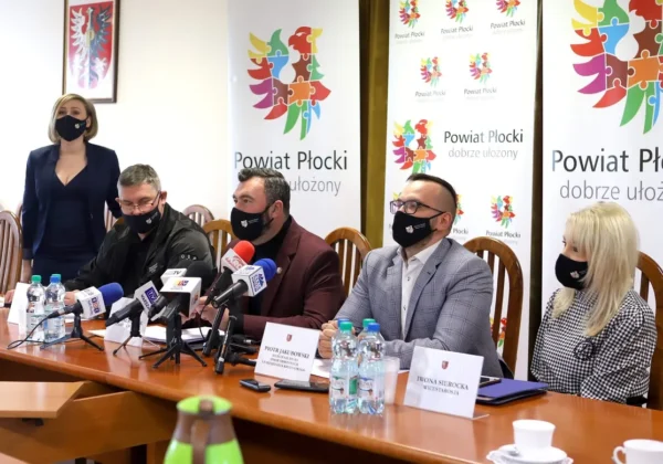 Konferencja prasowa podsumowująca sytuację przeciwpowodziową w Powiecie Płockim, podczas której pięć osób siedzi przy stole z mikrofonami i banerami Powiatu Płockiego w tle.