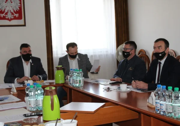 Czterech mężczyzn w maseczkach bierze udział w posiedzeniu Powiatowego Zespołu Zarządzania Kryzysowego ds. ptasiej grypy, siedząc przy stole w sali konferencyjnej z dokumentami i butelkami wody.