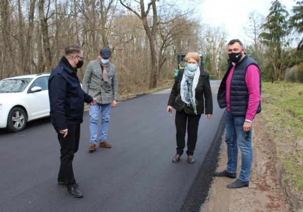 Czterech ludzi w maseczkach stoi na świeżo wyasfaltowanej drodze podczas przebudowy drogi w Powiecie Płockim.