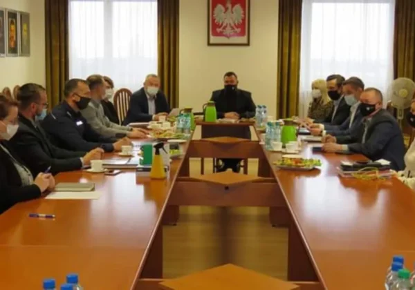 Uczestnicy posiedzenia Zarządu Powiatu Płockiego siedzą w maseczkach przy długim stole w sali konferencyjnej, a na ścianie wisi godło Polski.