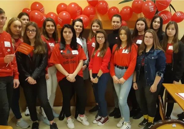 Grupa uczniów ósmej klasy stoi razem w szkolnej sali, ubrani na czerwono, z czerwonymi balonami w tle.