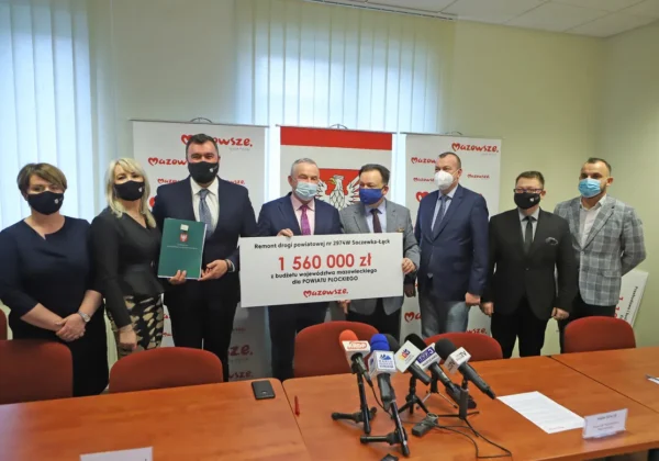 Grupa urzędników i samorządowców stoi w sali konferencyjnej, prezentując duży czek o wartości 1 560 000 zł na remont drogi powiatowej nr 2974W w Powiecie Płockim.