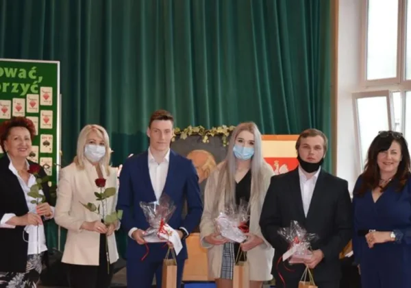 Grupa osób na scenie podczas uroczystości wręczania świadectw ukończenia LO i technikum w Zespole Szkół im. Stanisława Staszica w Gąbinie w roku szkolnym 2020/2021, trzymają kwiaty i upominki.