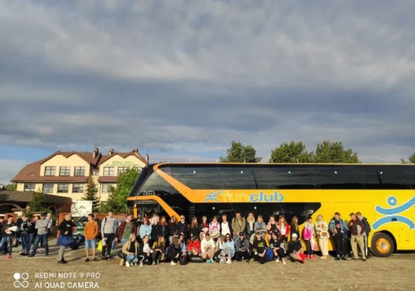 Duża grupa uczniów i nauczycieli stoi przed żółto-czarnym autobusem na placu przed szkołą podczas programu Erasmus 2021 – „Doskonalenie zawodowe” w Grecji.