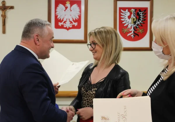 Podczas XXVI sesji Rady Powiatu wręczany jest dokument w trakcie apelu do władz państwowych, a w tle widoczne są herby powiatu.