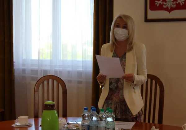 Kobieta w białej marynarce i maseczce trzyma kartkę z dokumentem podczas posiedzenia Powiatowej Rady Rynku Pracy w sali konferencyjnej.