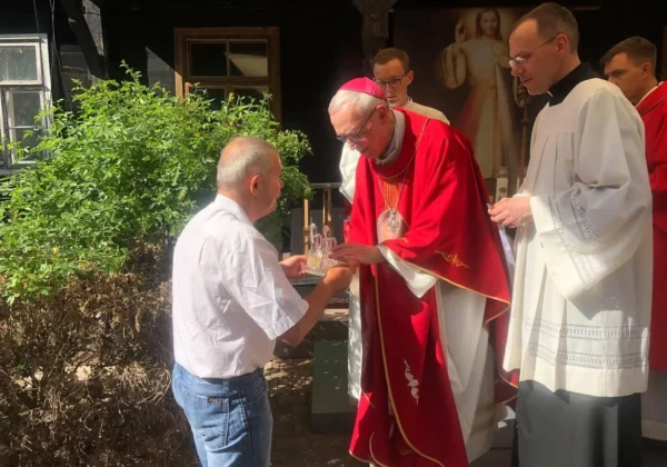 Ksiądz w czerwonej liturgicznej szacie wręcza upominek mężczyźnie podczas Imienin Antoniego, patrona Domu Pomocy Społecznej w Brwilnie.