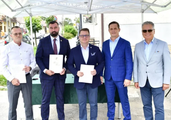Pięciu mężczyzn w garniturach stoi pod białym namiotem w Bodzanowie, trzymając dokumenty podczas oficjalnej prezentacji dotyczącej remontu głównej drogi.