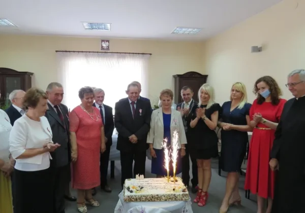 Grupa mieszkańców gminy Brudzeń Duży stoi wokół tortu z zapalonymi iskrami, świętując Złote Gody.