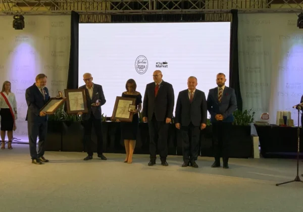 Na scenie podczas jubileuszu 150-lecia PSS Zgoda w Płocku grupa osób w garniturach trzyma ramkowe certyfikaty, a w tle wyświetlają się logotypy Zgoda i Top Market.