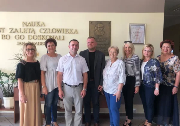 Grupa radnych Powiatu Płockiego podczas wizyty w Zespole Szkół w Wyszogrodzie stoi wspólnie w holu obok pamiątkowej tablicy.