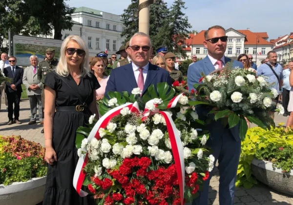 Grupa płockich mieszkańców składa biało‑czerwone wieńce przed kolumnowym pomnikiem z orłem na szczycie podczas uroczystości upamiętniającej bohaterów 1920 roku.
