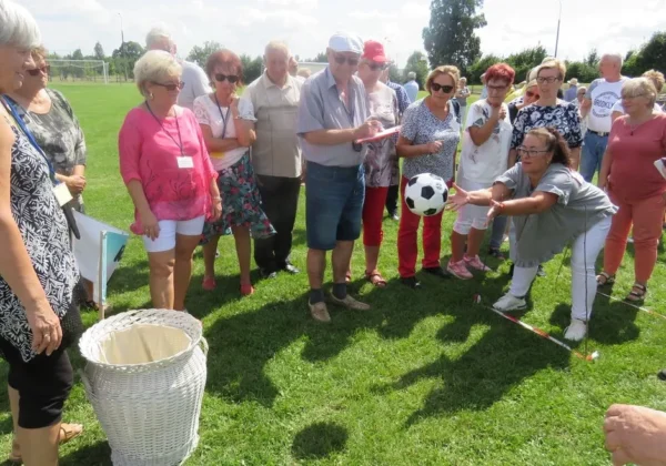 Grupa seniorów na zielonym boisku podczas Olimpiady Seniorów, obserwująca kopnięcie piłki.