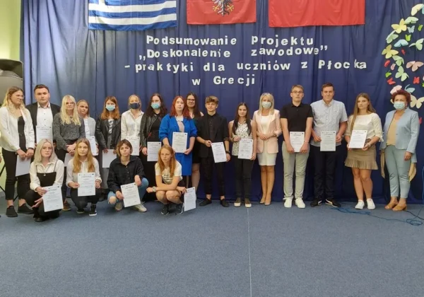 Grupa uczniów i nauczycieli Zespołu Szkół im. Leokadii Bergerowej w Płocku stoi na scenie, trzymając certyfikaty podczas podsumowania projektu Erasmus+ dotyczącego praktyk w Grecji.
