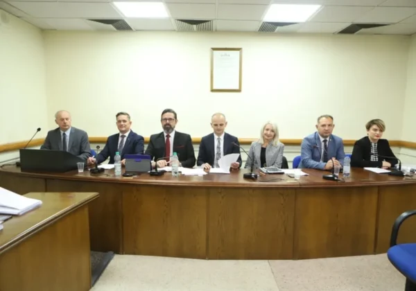 Grupa siedmiu urzędników w garniturach siedzi przy długim drewnianym stole z mikrofonami i dokumentami podczas XXVIII sesji Rady Powiatu w Płocku.