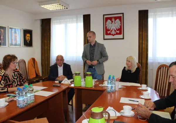 Grupa uczestników spotkania Powiatowej Rady Rynku Pracy w sali konferencyjnej; stojący mężczyzna przemawia, w tle wisi godło Polski.