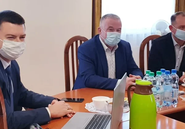 Trzech mężczyzn w maseczkach siedzi przy stole podczas spotkania samorządowego dotyczącego inwestycji w gminie Stara Biała, z laptopem, filiżankami i butelkami wody.