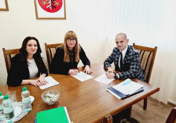 Trzy osoby siedzą przy stole w urzędowym pokoju i podpisują dokumenty dotyczące planowanej nowej ścieżki rowerowej w Gminie Słupno.