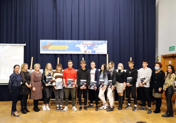 Grupa uczestników i opiekunów na scenie podczas gali projektu Czas na Staż Vol. II z programu Erasmus+, z certyfikatami w dłoniach.