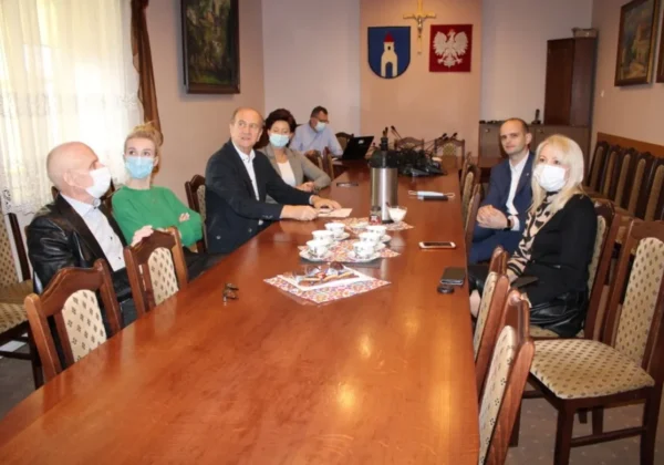 Grupa urzędników Powiatu Płockiego podczas roboczej wizyty w Gminie Gąbin, siedzą przy długim stole konferencyjnym w sali z herbami na ścianie, wszyscy w maseczkach.
