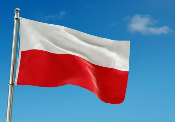 Flaga Polski biało-czerwona powiewa na maszcie na tle błękitnego nieba.