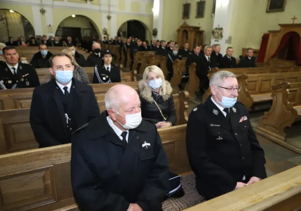 Uczestnicy XI Płockich Zaduszek Strażackich siedzą w drewnianych ławkach kościoła, wśród nich strażacy w mundurach i osoby w maseczkach.