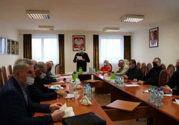 Uczestnicy Związku OSP RP w Płocku siedzą przy długim stole konferencyjnym podczas pierwszego posiedzenia Prezydium nowej kadencji, prowadzący stoi z kartkami, wszyscy mają maseczki.