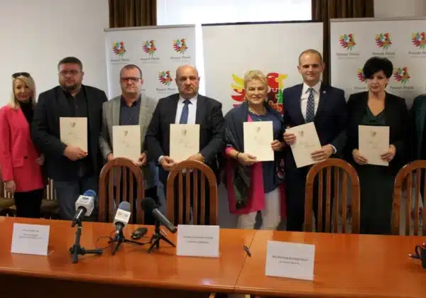 Na zdjęciu przedstawiono uroczystość podpisania dokumentów przez przedstawicieli Międzypowiatowego Ośrodka Wsparcia dla osób potrzebujących, odbywającą się w sali konferencyjnej z logo Powiatu Płockiego w tle.