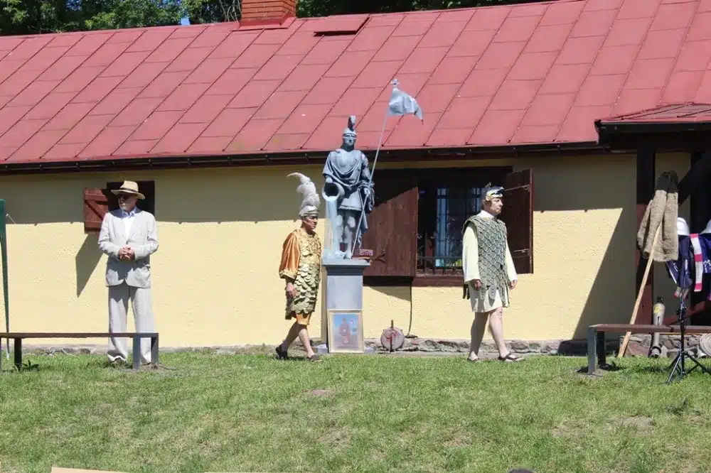 Na zdjęciu widać trzy osoby przebrane w historyczne stroje obok pomnika, z okazji 100-lecia Ochotniczych Straży Pożarnych w powiecie płockim.