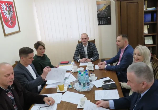 Grupa siedmiu osób w formalnych ubraniach siedzi przy stole w sali posiedzeń, omawiając dokumenty podczas posiedzenia Zarządu Powiatu Płockiego.