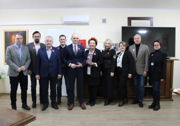 Grupa kilkunastu urzędników Powiatu Płockiego w garniturach i eleganckich ubraniach stoi razem na zdjęciu podczas posiedzenia Zarządu Powiatu Płockiego, we wnętrzu z dużym telewizorem w tle.