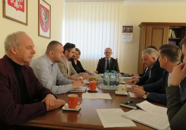 Grupa urzędników i przedstawicieli samorządu siedzi przy długim stole w sali konferencyjnej podczas posiedzenia Zarządu Powiatu Płockiego.
