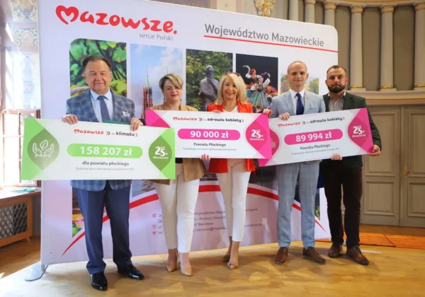 Pięć osób stoi na scenie i trzyma duże plakiety z kwotami dofinansowania w programach Mazowsze dla klimatu i zdrowia kobiet, na tle baneru z napisem Województwo Mazowieckie.