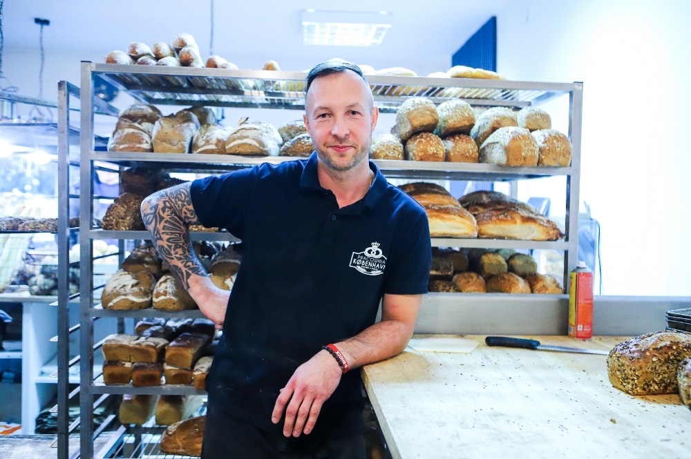 Piekarz oparty o blat, w tle półki z pieczywem