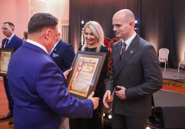 Podczas jubileuszu 25-lecia Samorządu Powiatu Płockiego mężczyzna wręcza dyplom kobiecie na scenie, w tle stoją inni uczestnicy.