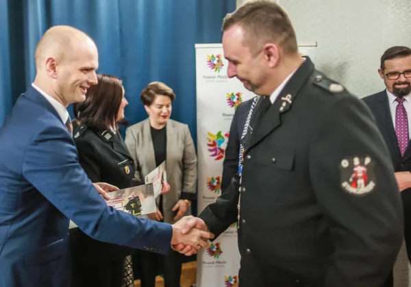 Podpisywanie umów w ramach VII edycji programu „Zakup sprzętu ratowniczego i umundurowania – 2024” dla jednostek OSP z powiatu płockiego, podczas którego osoba w garniturze ściska dłoń strażakowi w mundurze.